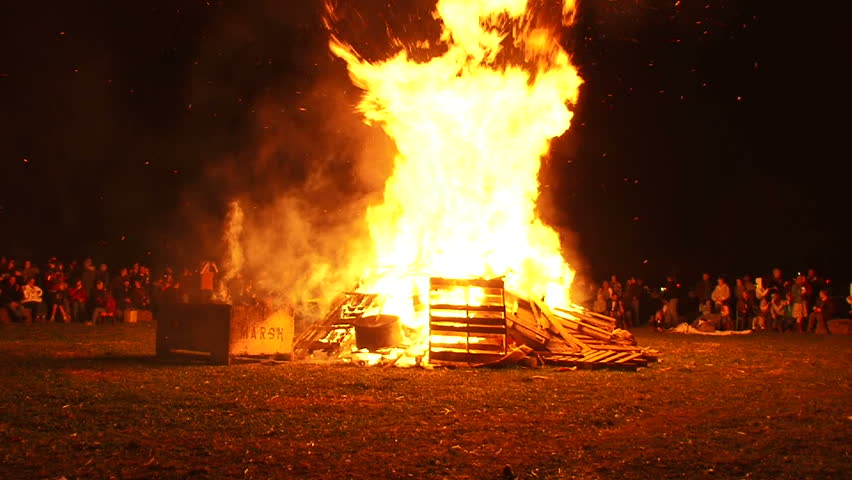 Many people watch as huge bonfire burns at night, time lapse.