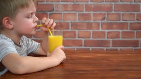 Cute little boy is drinking orange juice from straw, hd video