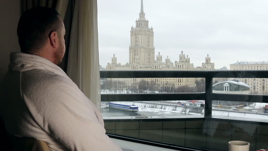 man sitting in a chair in the hotel room and looks at morning city
