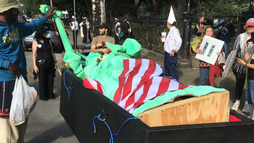 NEW ORLEANS, LOUISIANA CIRCA JANUARY 2017 - Activist interacts with fallen lady statue of liberty in coffin with american flag at anti Donald Trump inauguration day protest march performance art Royalty-Free Stock Footage #24512873