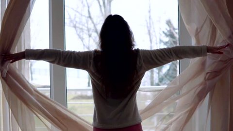 Young woman in sleeping costume opening the curtains in the morning at home