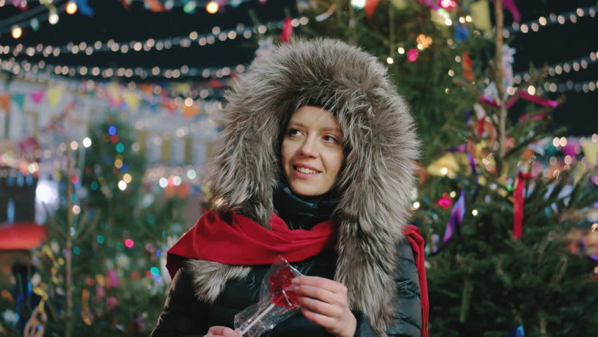 European woman with lollipop smiles in winter park.
