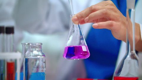 Lab scientist pouring liquid in lab flask. Close up of female scientist doing laboratory experiment. Lab worker hands doing laboratory testing with chemical liquid in beaker