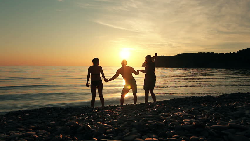 Group of people dancing on the beach at sunset, group of happy young people