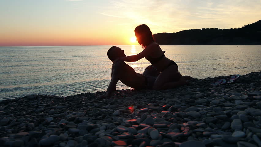 Two young lovers on a beach on sunset background