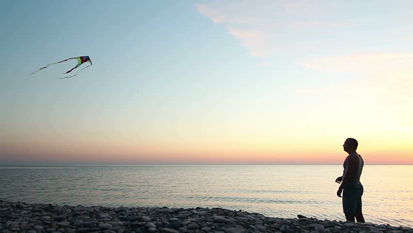 Man flies a kite on the shore of the sea at sunset at summer time