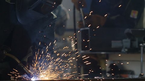 welder in equipment works with welding machine inside production workshop bright sparks fly around in darkness