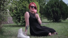 red-haired girl in a black dress with candy and rollers sitting on the grass