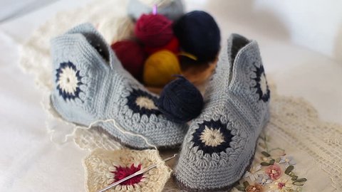 Soft, knitted woolen slippers. Near skeins of yarn and knitting needles. Close up