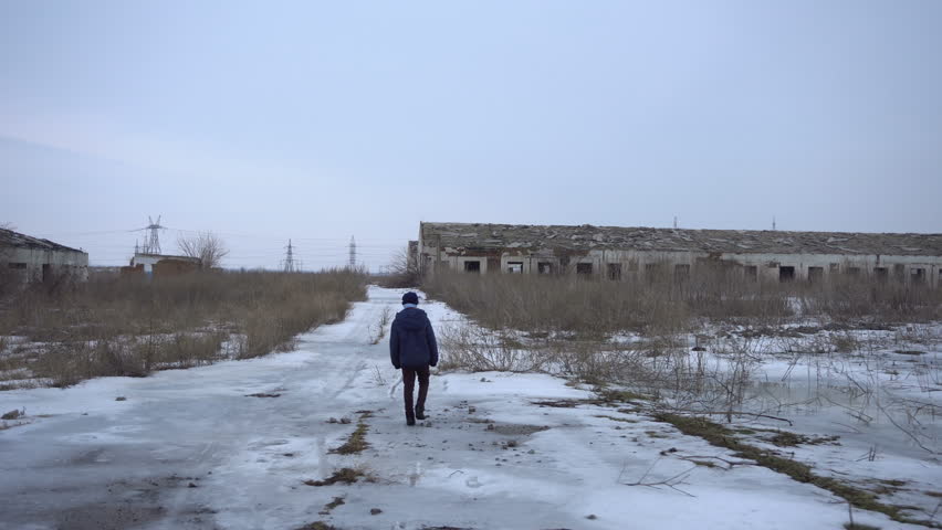 The boy is near the old ruined farm in winter. Shooting with Steadicam 4K