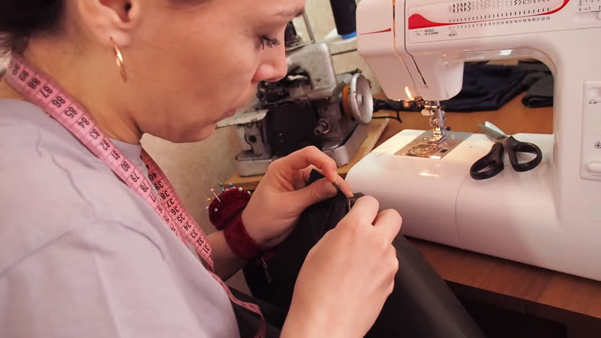 Seamstress work on the sewing machine. Girl sits at the table and scribbling on the sewing machine. A woman in a gray T-shirt. White sewing machine.