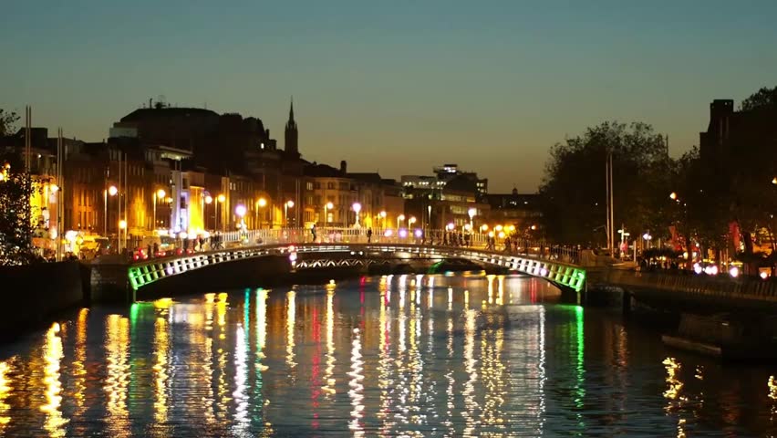 River Liffey and the famous Hapenny Bridge, night view cityscape, Dublin, Ireland. Yellow and green night lights are reflecting on the water surface. Christmas time in Europe.