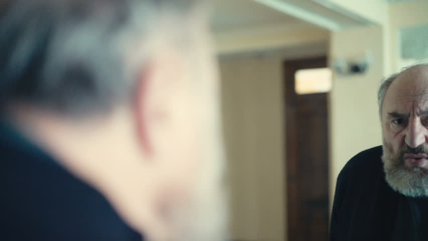 Handsome old man makes faces in front of the mirror in 4K