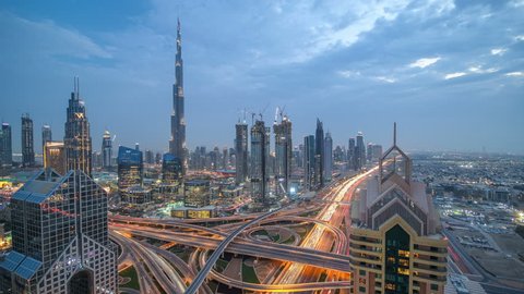 View on modern skyscrapers and busy evening highways day to night transition timelapse in luxury downtown of Dubai city. Top aerial view from tower rooftop. Road junction traffic. Dubai, United Arab