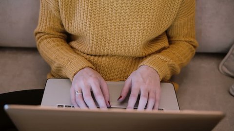 Female hands working on laptop sitting on the couch at home and typing. Fop view of woman holding computer.