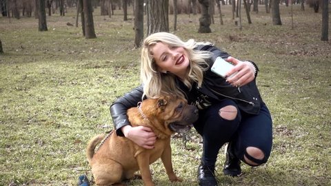 KHERSON, UKRAINE - MARCH 03, 2017: Young Woman taking Photo Selfie with Mobile Phone Playing Sharpei Dog In Spring Park
