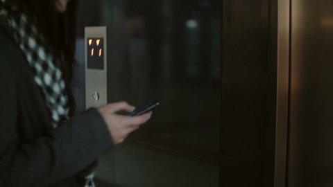 Woman press the button in the elevator and wait. Female standing in office and using smartphone, touching the screen.