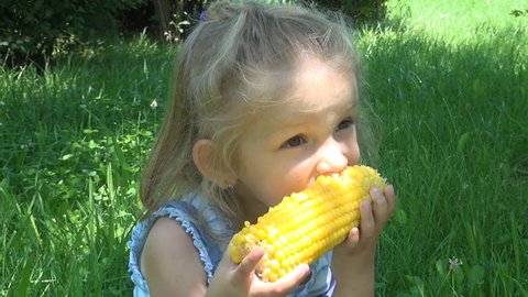 A Small Child Eating a Boiled Corn on a Bench in Park