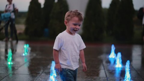 Attractive little boy running trough fountain and touching water jets. Child having fun on hot summer day.