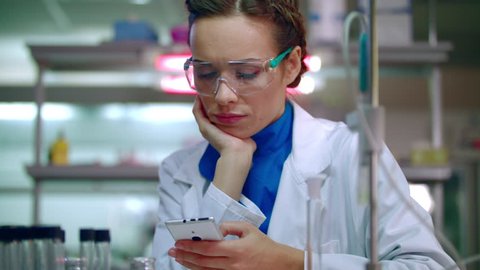Medical scientist typing on phone in lab. Lab technician using phone in laboratory. Lab woman texting on smartphone. Medical researcher using mobile phone in medicine laboratory