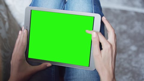 Young Woman sitting on the floor uses tablet PC with pre-keyed green screen. Few types of motion - scrolling up and down, tapping, zoom in and out. Perfect for screen compositing. 10bit ProRes 444
