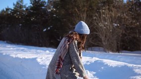 A young girl having fun in the snowy day, it is warmly dressed in a gray coat, a blue knitted hat. The girl is laughing, fooling around and having fun in the woods, tossing up a handful of snow.