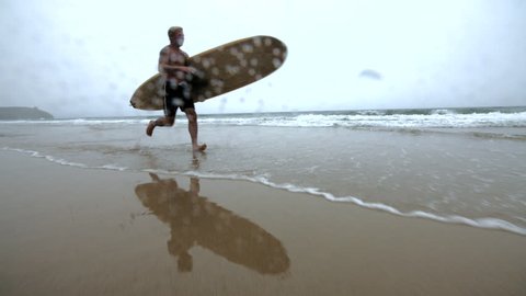 Mature Surfer Running Along the Ocean Edge.