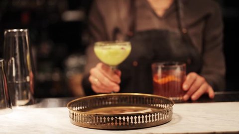 alcohol drinks, people and luxury concept - barmaid putting glasses of cocktails to tray at bar