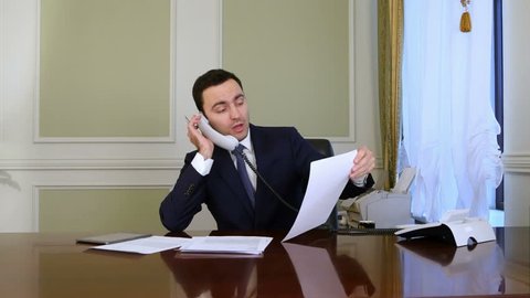 Young confident successful businessman working in modern office analyzing business by phone conversation