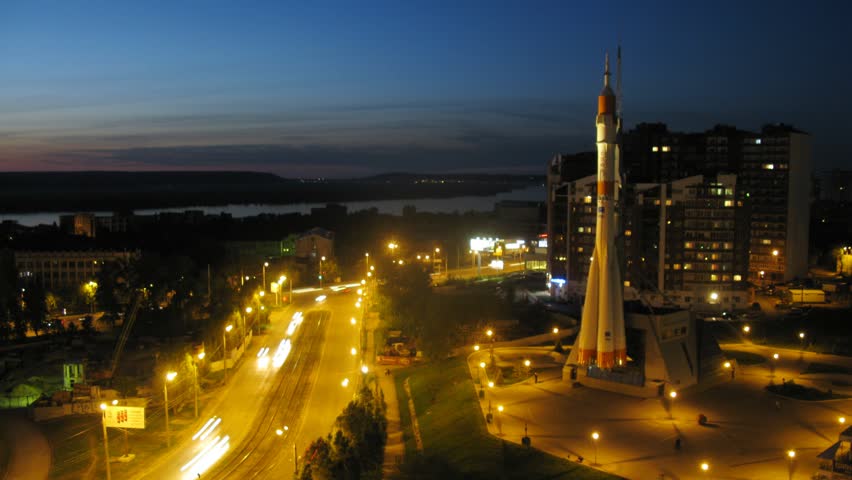 Monument rocket stands at mountain top against city landscape of Samara at night, time lapse