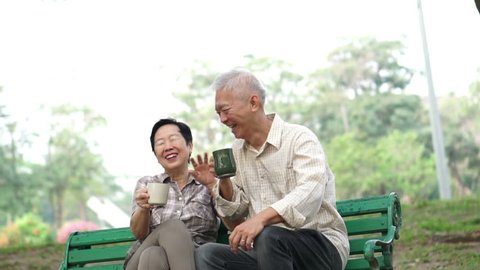 Slow motion happy Asian senior elder couple sitting and drinking tea, coffee morning park. Having conversation and showing love