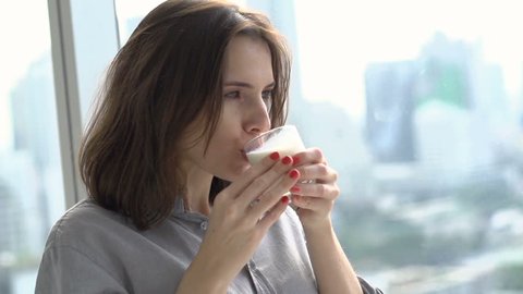 Happy, young woman drinking milk standing by window at home, super slow motion 240fps
