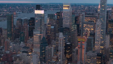 AERIAL HELI SHOT: Huge shining glassy skyscrapers, lit contemporary office buildings and luxury condo towers rising above low-rise blocks of flats in Midtown Manhattan New York City at pik light dawn