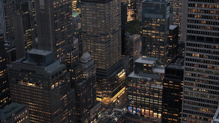 AERIAL HELI SHOT: Flying past lit with lights iconic Chrysler Building rising above modern office buildings and busy crowded New York streets after the sunset. Industry machinery in construction pit Royalty-Free Stock Footage #24621593
