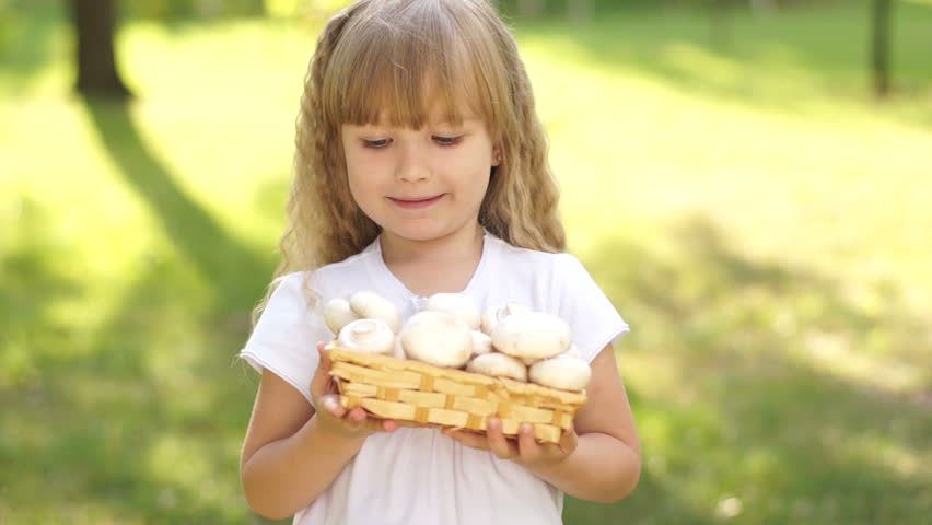 Little girl with a basket of mushrooms. She laughing and looking at camera
