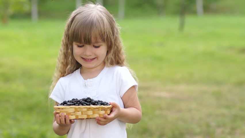 Child holding a basket of black currant. She shows the tongue
