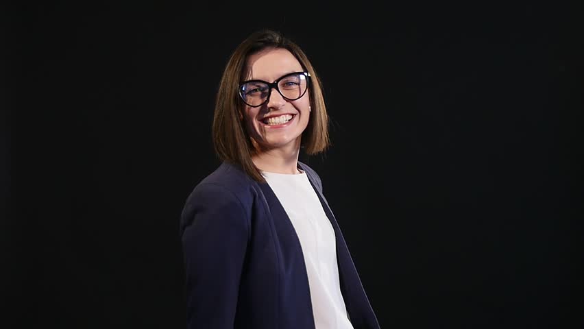 Close up Happy Young Woman, Wearing Eyeglasses, Showing Toothy Smile at the Camera Against Gray Wall Background.