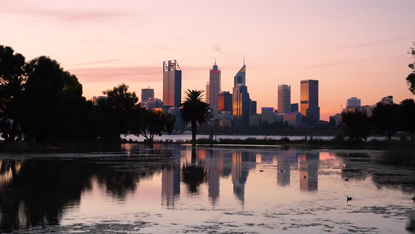 The buildings of Perth city reflect in a lake near the Swan River at sunset. Western Australia, Australia.
