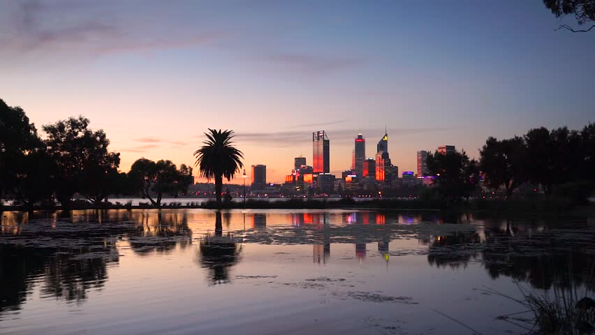 The buildings of Perth city reflect in a lake near the Swan River at sunset. Western Australia, Australia.