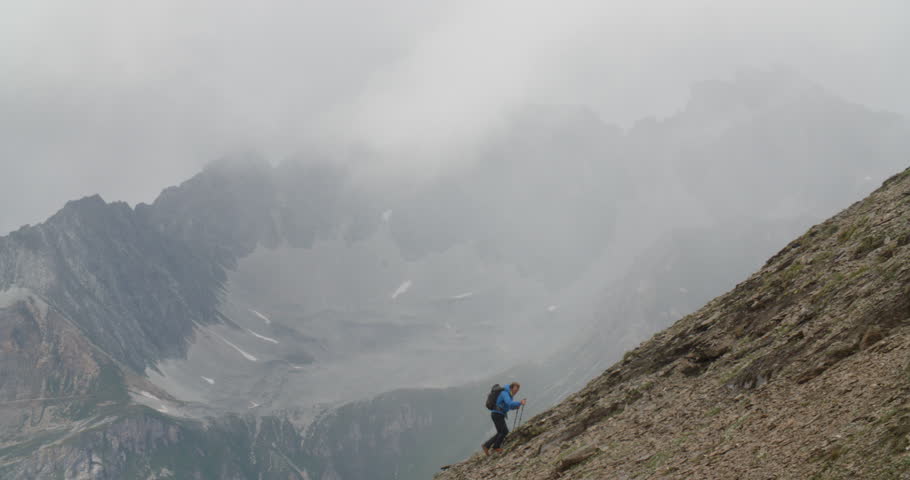 Mountaineer climbing up steep alpine slope with bad weather closing in.