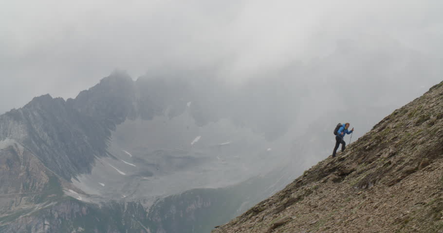 Mountaineer climbing up steep alpine slope with bad weather closing in.
