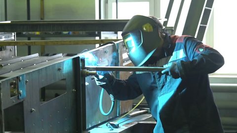 Man welder welds the parts of structure in slow motion. Guy in orange protective mask working. Good skill. Cool welder makes a lot of sparks. Man in glasses makes dangerous job slowmotion welding.