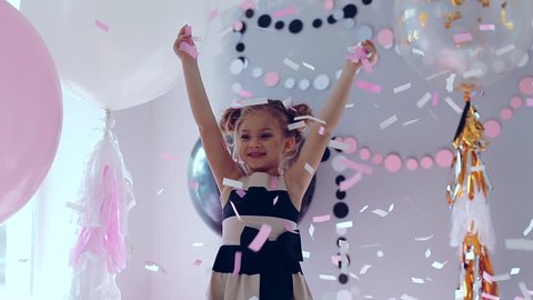 Little girl jumping and having fun celebrating birthday. Portrait of a child throws up multi-colored tinsel and confetti. Positive emotions. Happy excited laughing kid under sparkling confetti shower