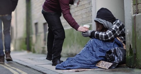 4k, Man hands over a hot drink to a homeless woman.