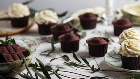 chocolate muffins, cupcakes with beige cream in a ceramic light plates on a white wooden background move left to right under the corner of the video