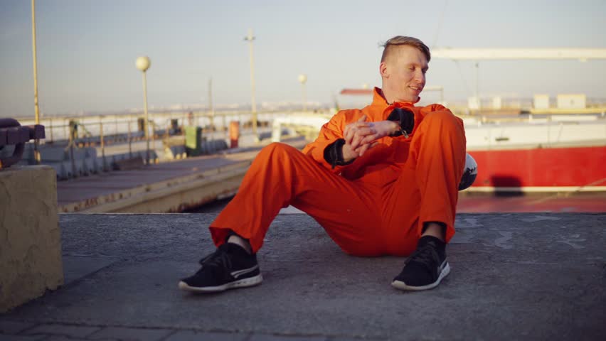 Young man in orange uniform sitting during his break by the sea in the harbor