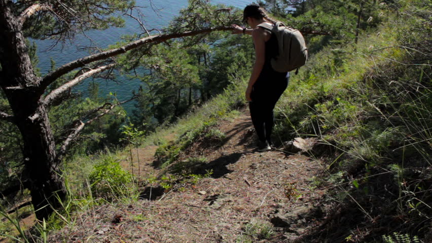 Girl coming down the steep mountainside to ocean. Young woman descend to the sea