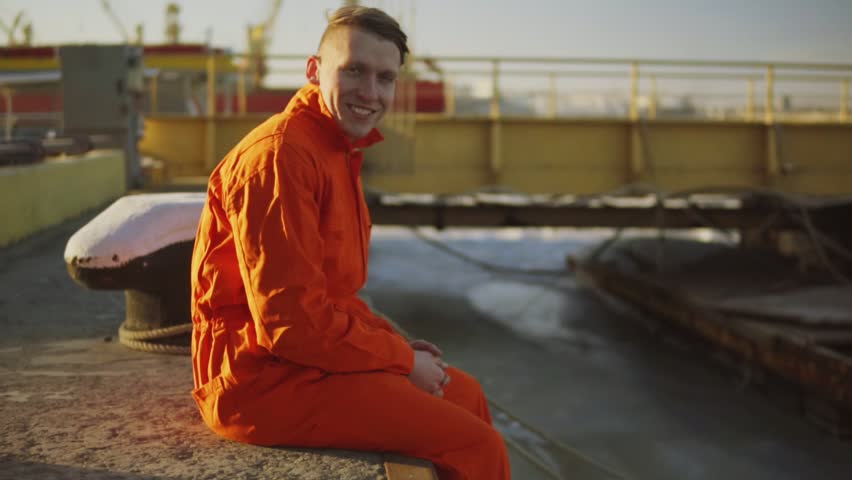 Portrait of young worker in orange uniform sitting during his break by the sea