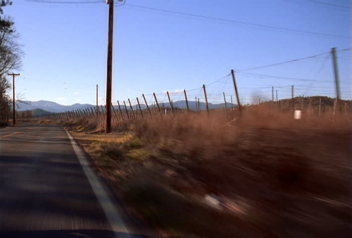 Hood-mount POV of car traveling on rural road near hop fields