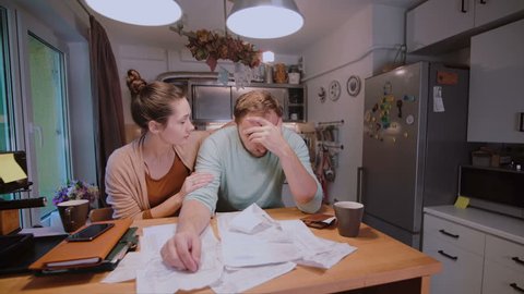 Young couple calculating bills in the kitchen at home. Woman try to calm sad and angry husband.